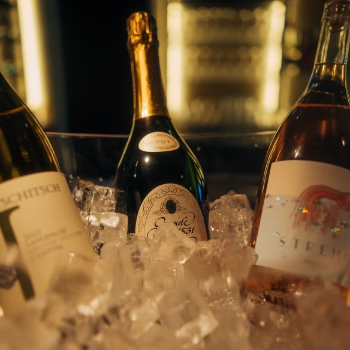 Nahaufnahme von drei Flaschen, darunter Champagner/Sekt, gekühlt in einem Eiskübel in einer dunklen Barumgebung.